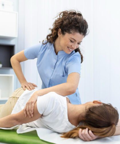Young woman doctor chiropractor or osteopath fixing lying womans back with hands movements during visit in manual therapy clinic Professional chiropractor during work
